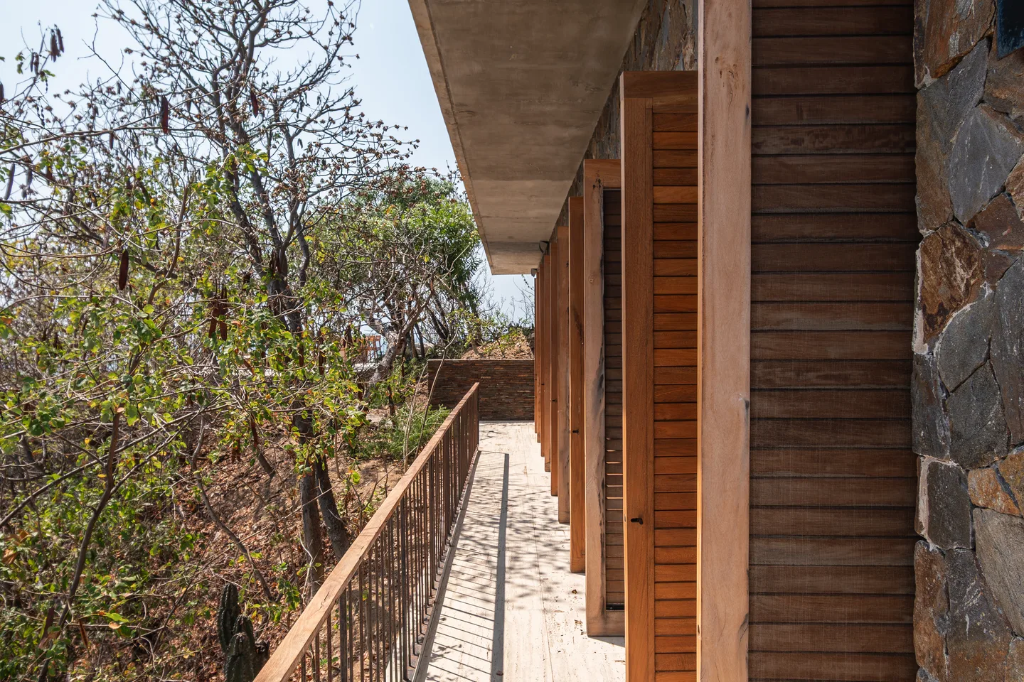 Pasarela de madera y fachada de persianas de Casa Chicatana entre los árboles — La Valise Mazunte