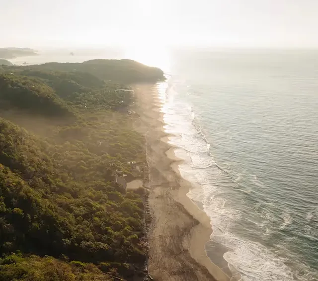 Aerial view of the long wild beach and surf beside El Torón Reserve at golden hour