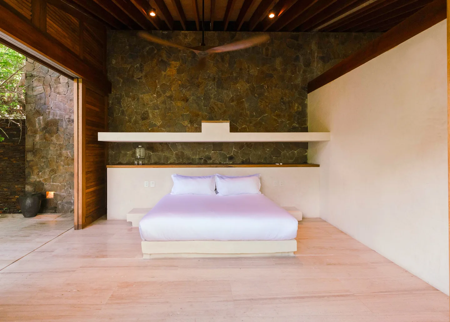 Cama king contra un muro de piedra en Suite Ceiba — La Valise Mazunte