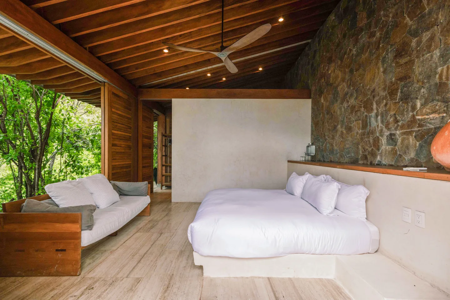 Suite Olas bedroom with sofa and wooden doors open to the trees — La Valise Mazunte