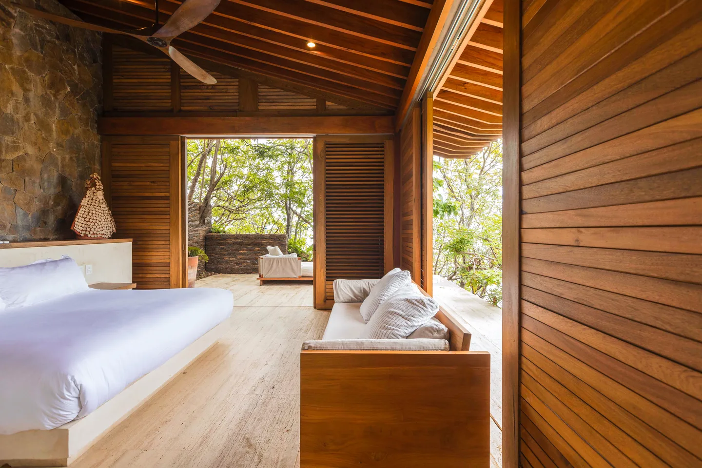 Cama y sofá en la Suite Mar Azul con puertas de madera abiertas al jardín — La Valise Mazunte