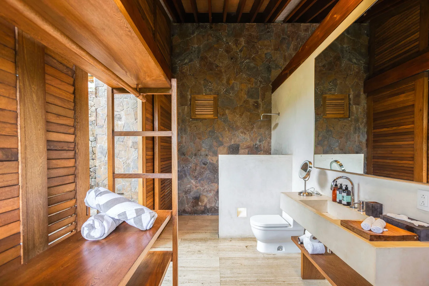 Baño de la Suite Mar Azul con tocador de madera y muro de piedra — La Valise Mazunte